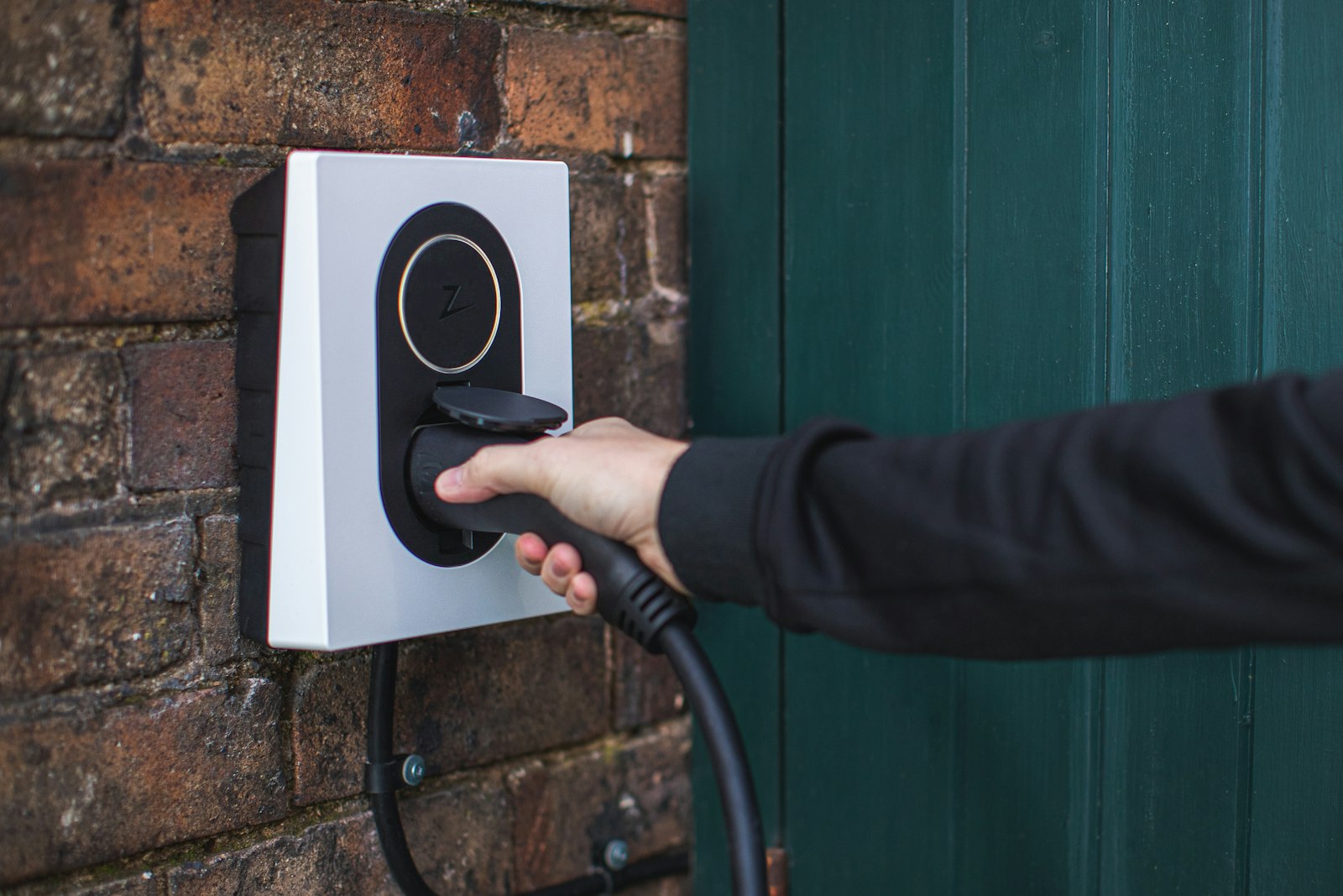 Hand steckt Ladekabel in eine Wallbox an der Hauswand